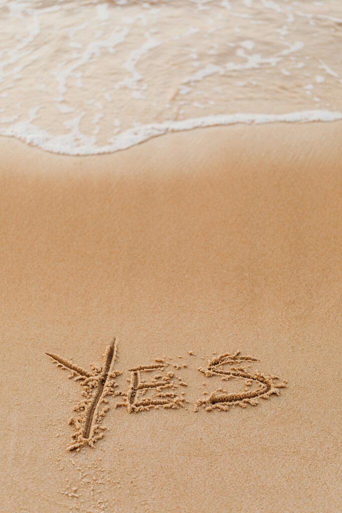 The word 'YES' written in sand near ocean waves on a beach.
